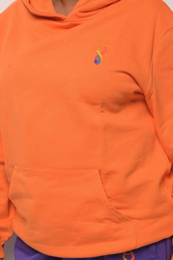 A person wearing an orange hoodie with a rainbow colored raindrop.