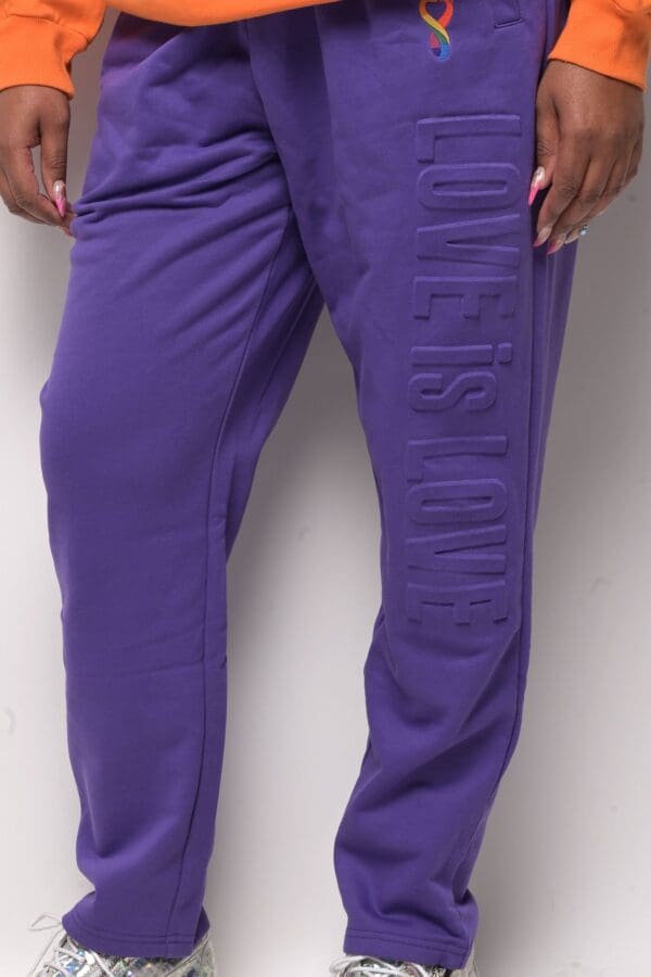 A person wearing purple pants standing next to a wall.