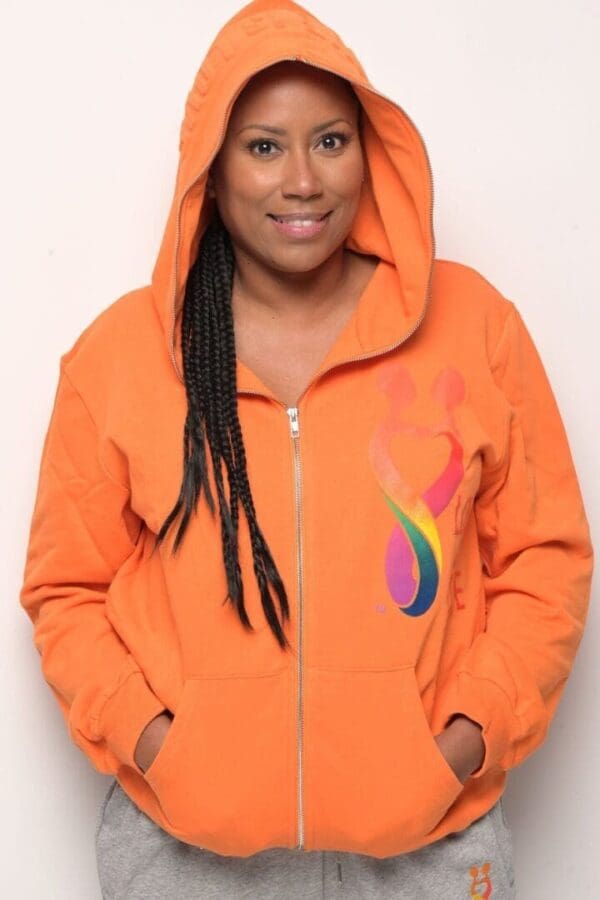 A woman wearing an orange hoodie with a rainbow design on the front.